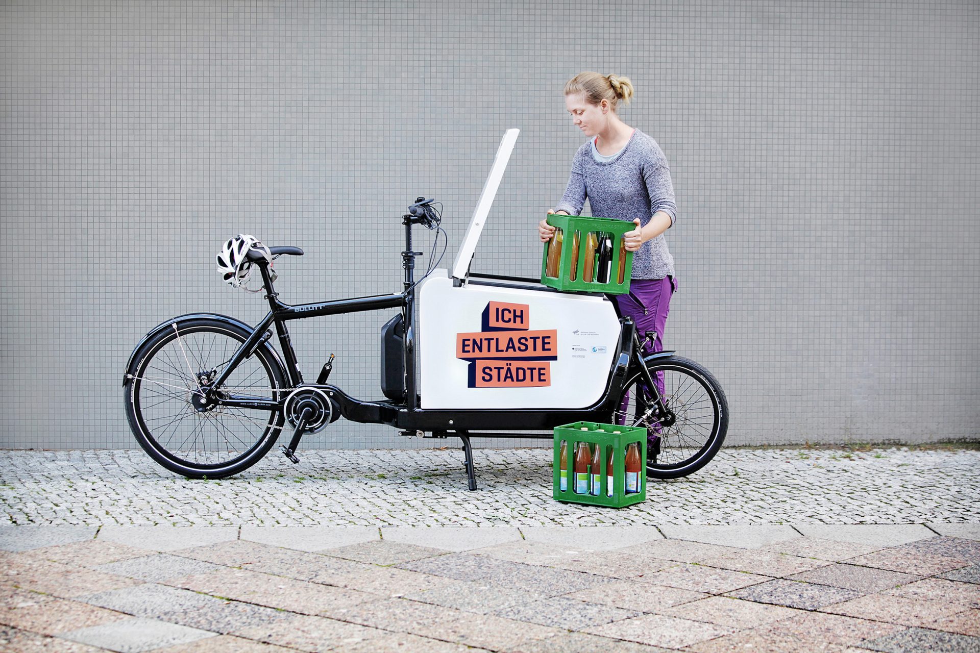 Eine Frau belädt ein Lastenrad mit Getränkekisten. Auf dem Rad ist 